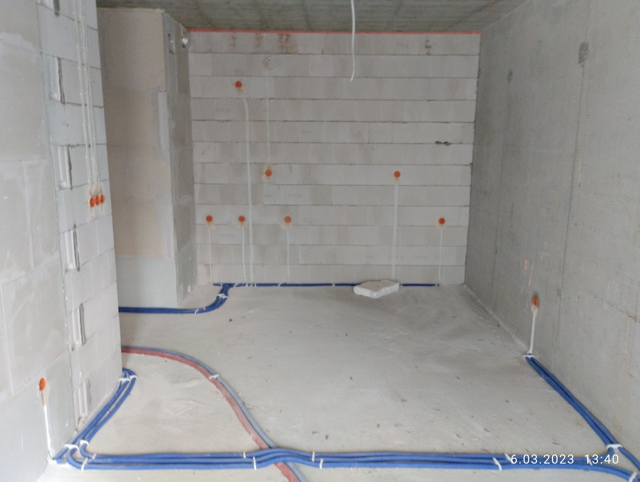 Surowy stan wnętrza w trakcie prac elektrycznych: widoczne przewody w peszlach ułożone wzdłuż ścian i wyprowadzenia kabli ze ścian, ściany z betonu komórkowego.
