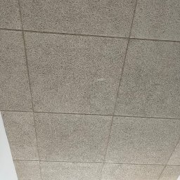 Fast Build by Roman Vynnyk - Sufit z paneli akustycznych o fakturze wełny drzewnej, widoczne łączenia między panelami, fragment okna w dolnej części kadru.