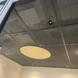 Metalowy sufit rastrowy z okrągłym panelem akustycznym i wbudowanym oświetleniem punktowym w nowoczesnym biurze.