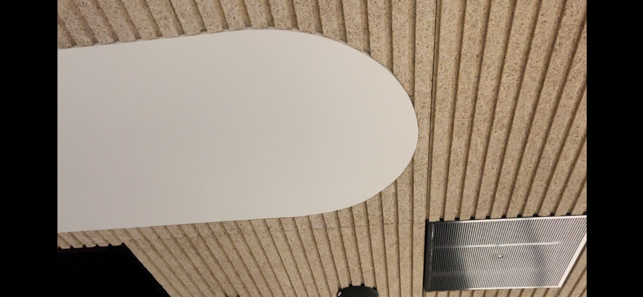 Zabudowa sufitowa z wełny drzewnej z elementem oświetleniowym o zaokrąglonym kształcie, widoczna kratka wentylacyjna.