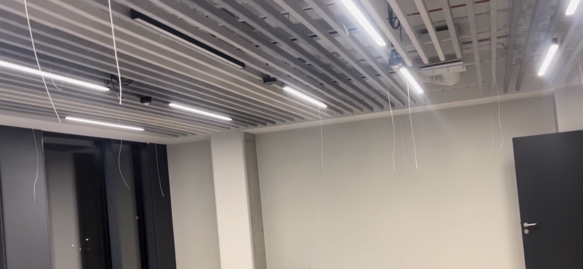 Montaż sufitu rastrowego z widocznymi przewodami zwisającymi z konstrukcji w biurze.