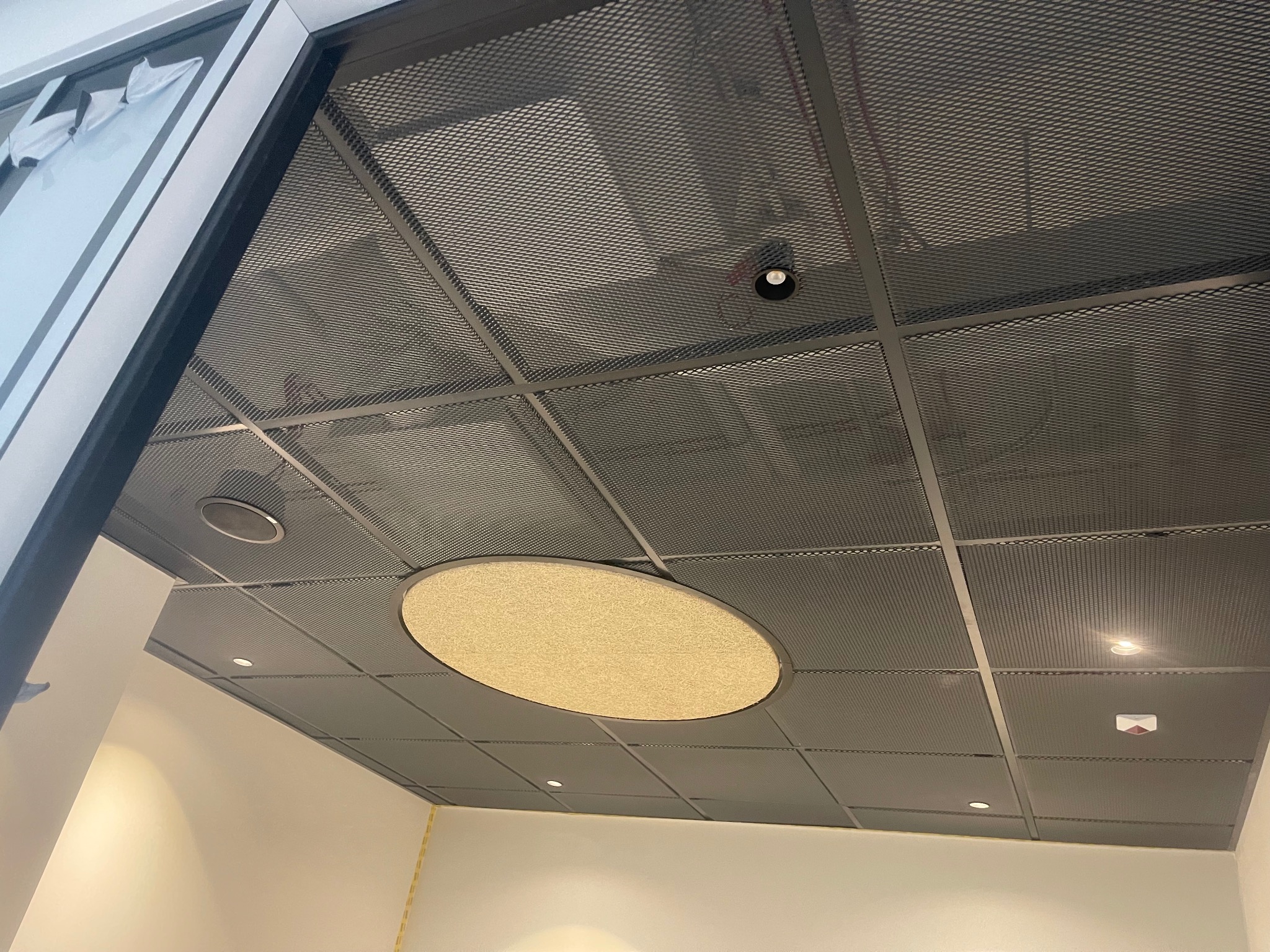 Metalowy sufit rastrowy z okrągłym panelem akustycznym i wbudowanym oświetleniem punktowym w nowoczesnym biurze.