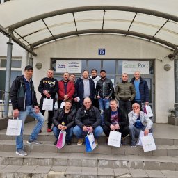 SAVRAN Sp.z o.o. - Grupowe zdjęcie pracowników budowlanych przed budynkiem biurowym GreenPort, trzymających torby z logo Siniat.