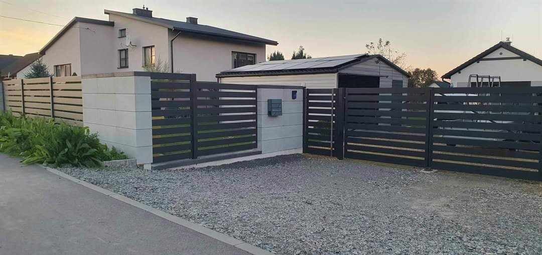 Nowoczesna posesja z ogrodzeniem panelowym w kolorze grafitowym, z poziomymi przęsłami, osadzonym na betonowych słupkach, brama wjazdowa przesuwna, szara kostka brukowa na podjeździe, dom...