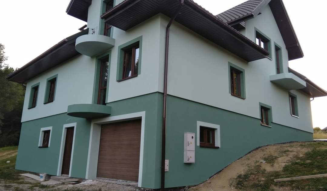 Dwukolorowa elewacja domu jednorodzinnego z brązowymi ramami okiennymi i garażem, widok z dołu.