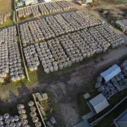 Widok z lotu ptaka na plac składowy z ułożonymi w rzędach workami z opałem, obok budynki gospodarcze, pojazdy i stosy drewna.