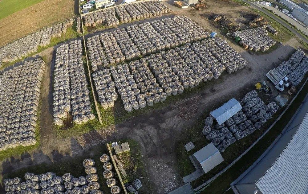Widok z lotu ptaka na plac składowy z ułożonymi w rzędach workami z opałem, obok budynki gospodarcze, pojazdy i stosy drewna.