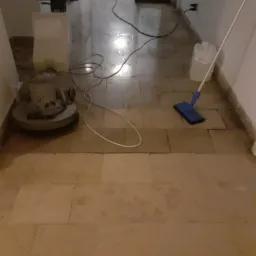 Polerka do podłóg i mop na mokro na korytarzu z kamienną posadzką w trakcie czyszczenia, widoczny także kanister z płynem i przewody zasilające