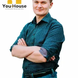 Mężczyzna w koszuli w kropki z założonymi rękami na białym tle, obok logo YouHouse z hasłem 'Znajdź dobre miejsce dla siebie'.