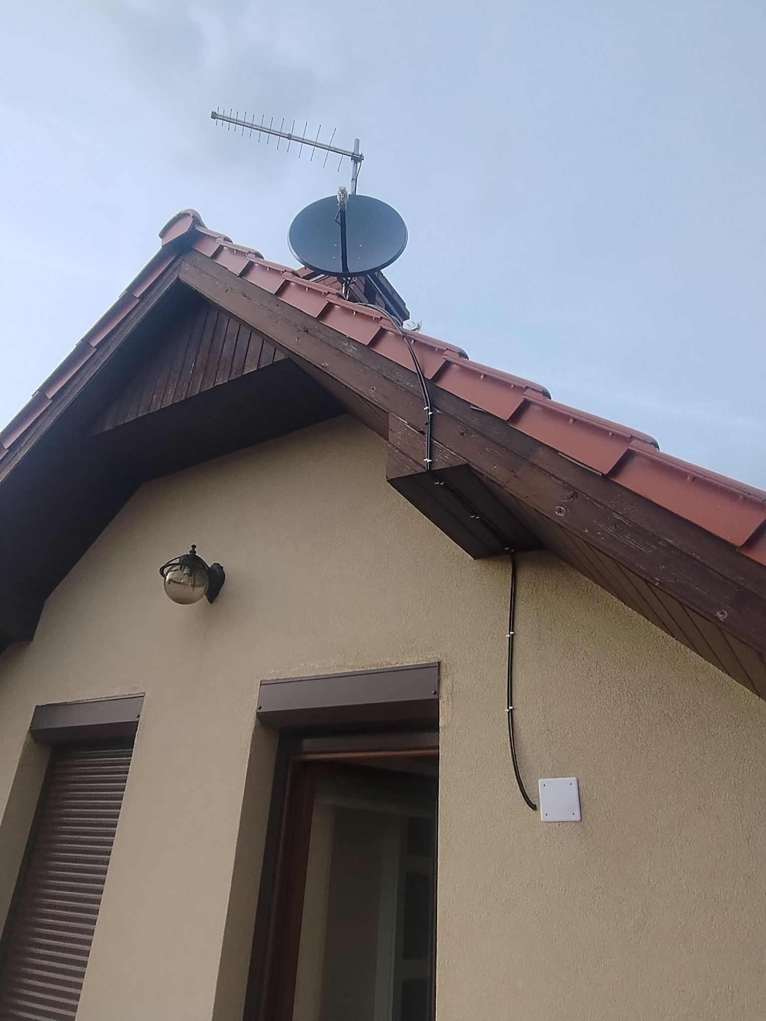 Antena satelitarna i naziemna zamontowane na dachu domu jednorodzinnego. Kable antenowe poprowadzone wzdłuż ściany budynku. Widok z dołu.