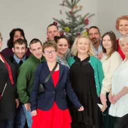 Grupowe zdjęcie zespołu pracownik&oacute;w odzieżowych na tle choinki, prezentujące r&oacute;żnorodność styl&oacute;w i ubrań.