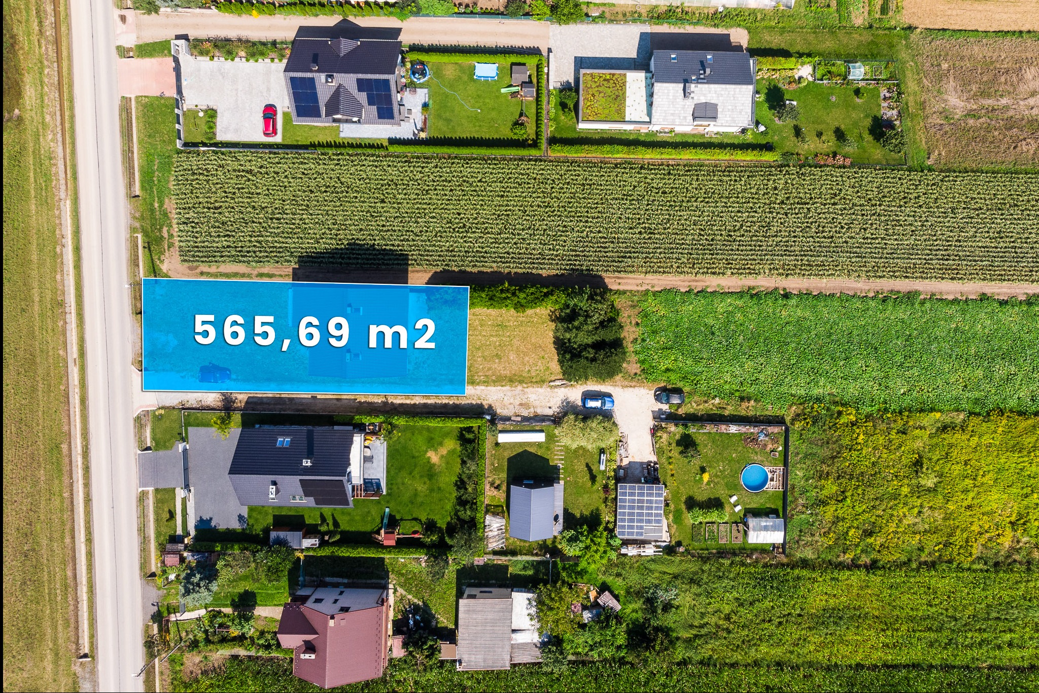 Widok z lotu ptaka na działkę z zaznaczonym obszarem 565,69 m2, otoczoną domami, polami uprawnymi i drogą.