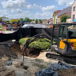 Kamil Dutkiewicz - Żółta koparka Volvo EC35C w trakcie prac ziemnych na ulicy miejskiej, wykop zabezpieczony czarną folią, w tle zabudowa miejska i błękitne niebo.
