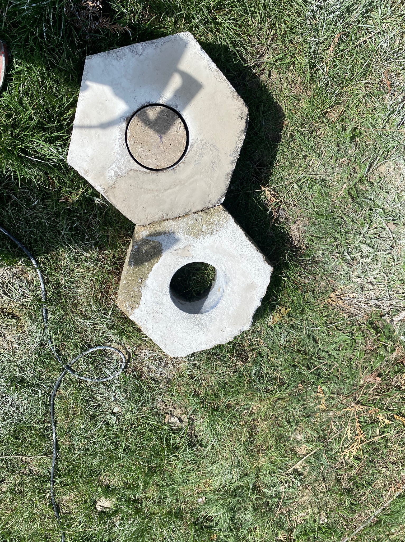 Dwa betonowe kręgi z otworem leżą na trawie, jeden z nich ma zamknięty otwór, prawdopodobnie dekiel.