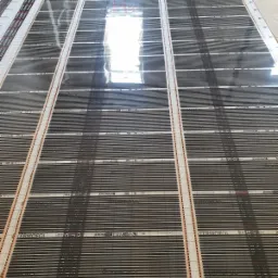 Rozłożone maty grzewcze pod ogrzewanie podłogowe, widoczne czarne paski grzejne na białej folii z nadrukiem 'TERMOFOL', przygotowane do zalania wylewką.