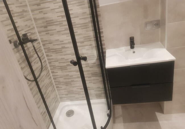 Nowoczesna łazienka z kabiną prysznicową z czarnymi profilami i armaturą oraz szafką pod umywalkę w kolorze grafitowym z białą umywalką nablatową.