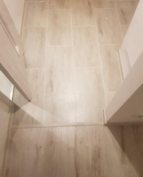 Jasne, prostokątne płytki podłogowe imitujące drewno, ułożone w korytarzu pomiędzy ościeżnicami drzwiowymi.