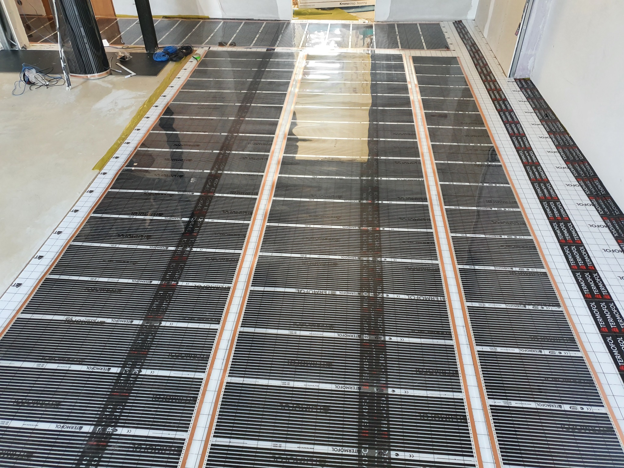 Rozłożone maty grzewcze Termofol na podłodze w trakcie montażu, widoczne przewody i taśma mocująca.