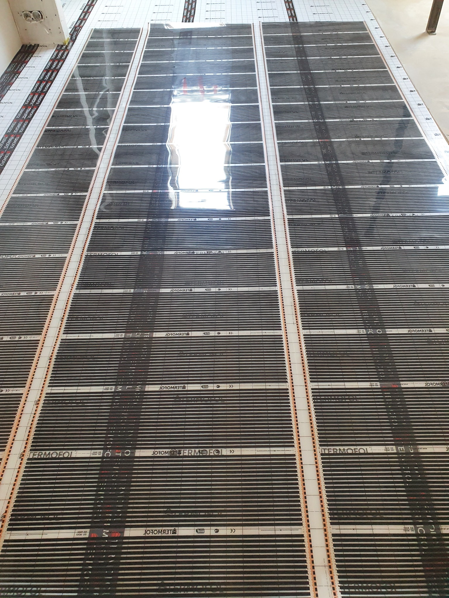 Rozłożona mata grzewcza pod panele podłogowe marki Termofol, widok z góry na ogrzewanie podłogowe przed montażem paneli z widocznym napisem Termofol.