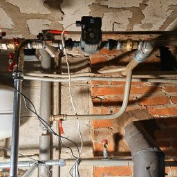 solar serwis dariusz borys - Szczegółowe ujęcie instalacji grzewczej z pompą obiegową i rurami w piwnicy w Krasnystawie. Widoczna surowa ściana z cegły i betonowy sufit.