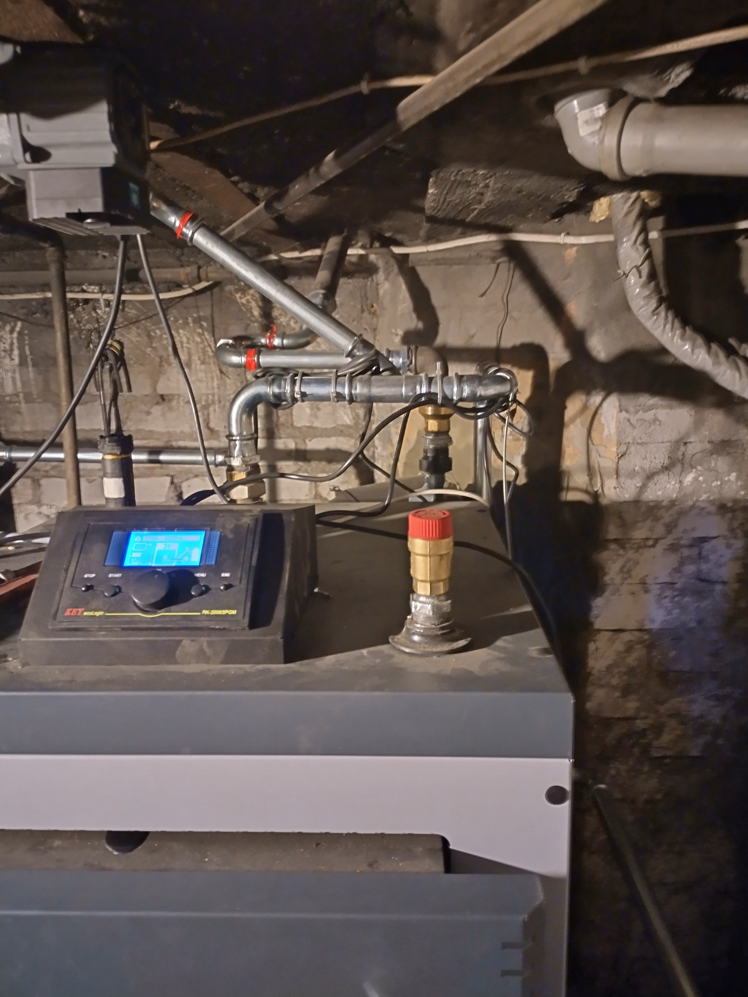 Nowoczesny piec CO z automatyką, widoczne rury instalacji grzewczej i czujniki. Instalacja w piwnicy, surowe ściany.