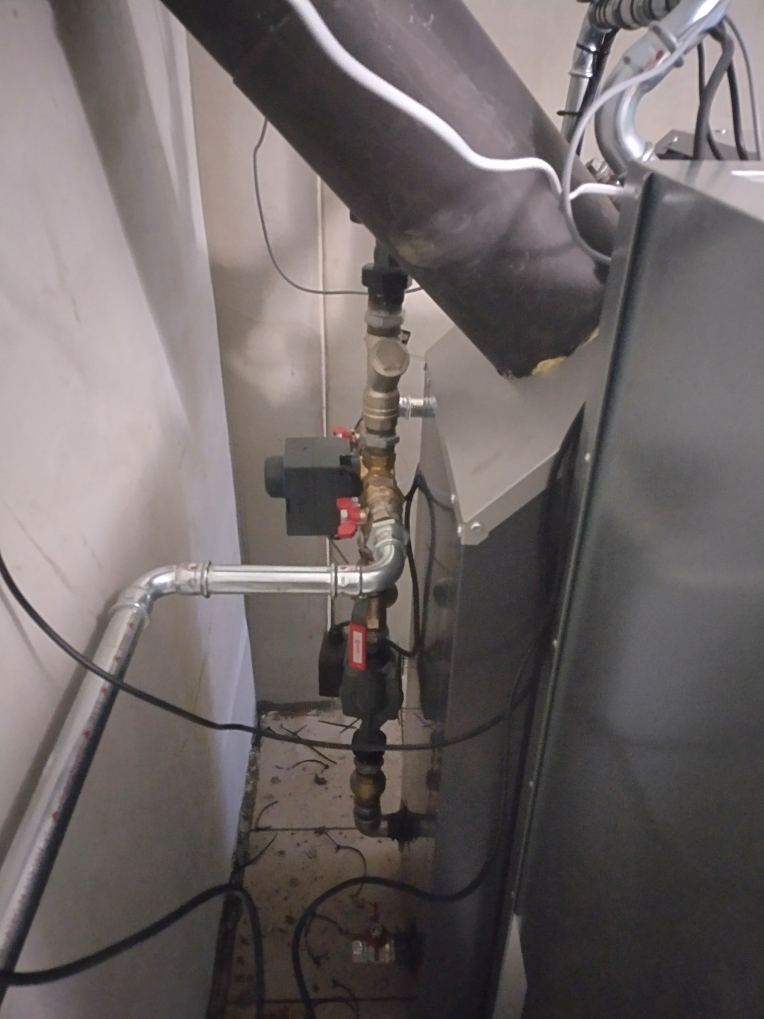 Szczegółowe ujęcie instalacji pieca CO z rurami, zaworami i czujnikiem, widoczne przyłącza i elementy montażowe w kotłowni.