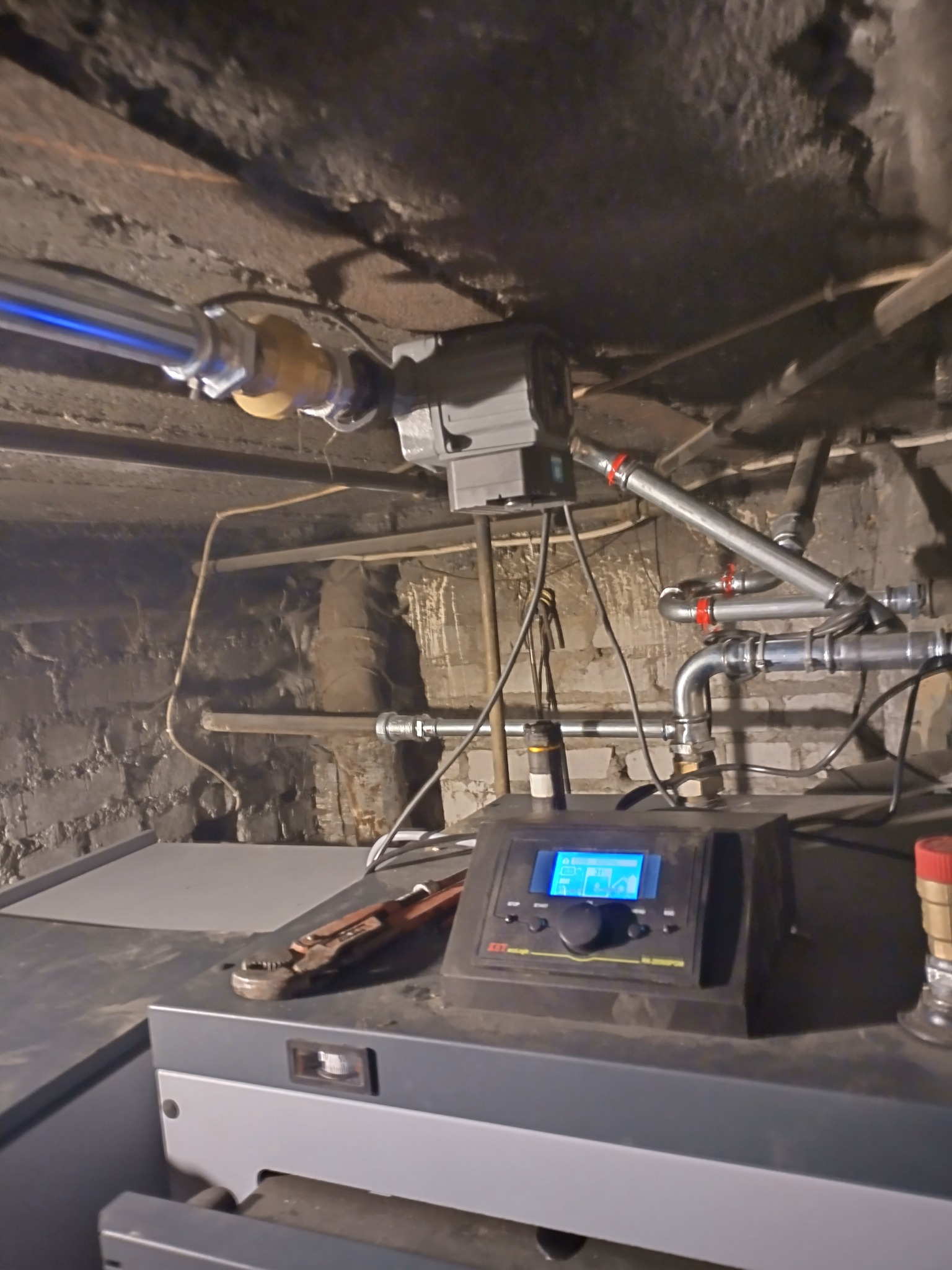 Zamontowany piec CO z widoczną instalacją hydrauliczną, rurami i pompą obiegową w kotłowni. Na piecu leży klucz do rur.