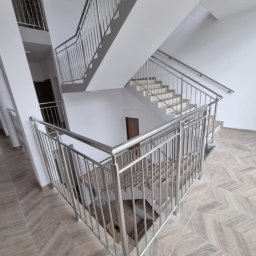 „Żelazny” Uslugi Spawalnicze - Wielopoziomowe schody z balustradami ze stali nierdzewnej, widok z góry, wzór parkietu na podłodze, minimalistyczny design, jasne wnętrze.