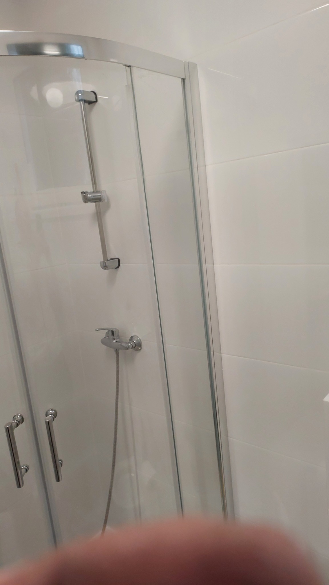 Szklana kabina prysznicowa z chromowanymi uchwytami i baterią, białe płytki na ścianach, ujęcie z bliska.