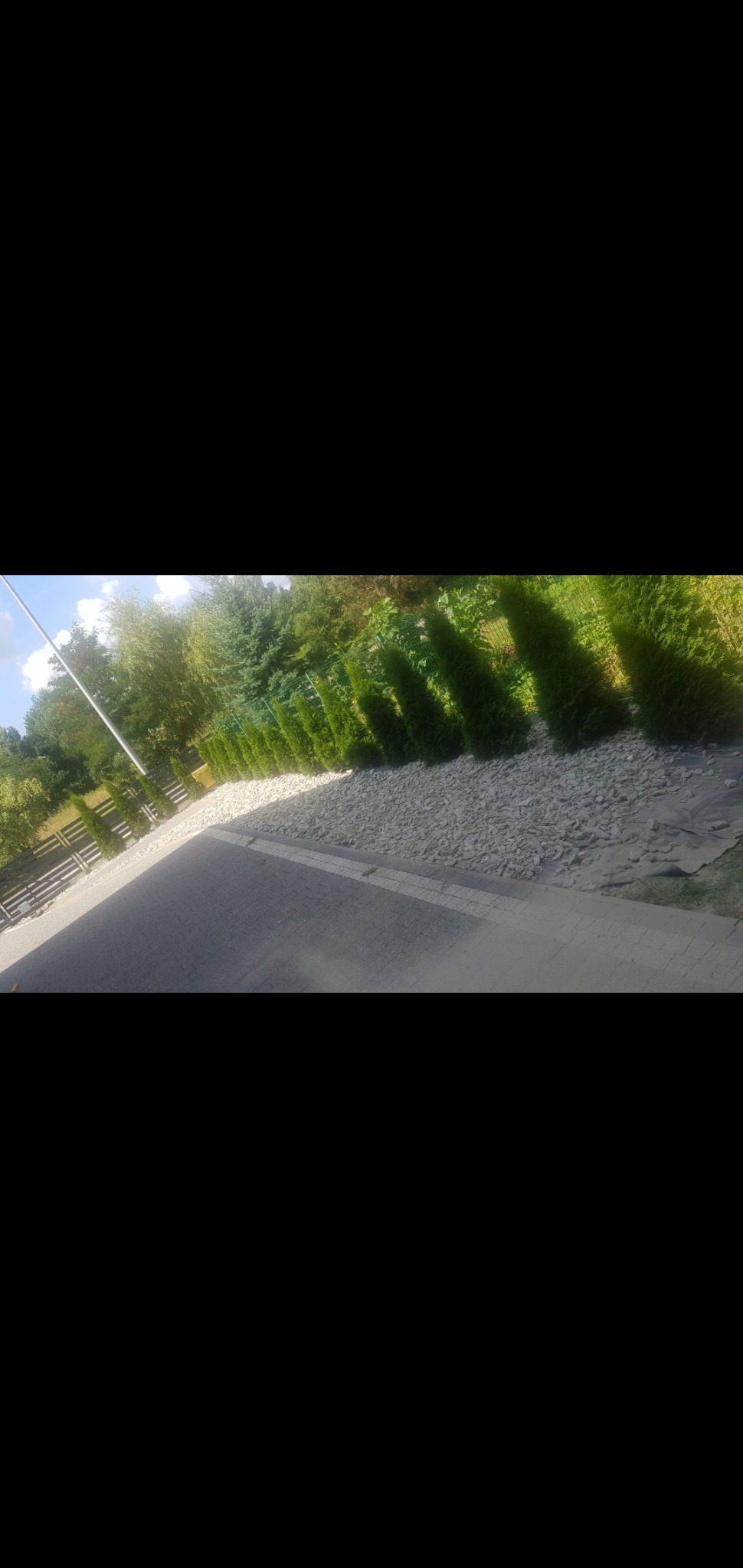 Świeżo ułożona kostka brukowa w Opolu sąsiaduje z rabatą wysypaną drobnymi kamieniami, za którą rosną równo posadzone, młode tuje.