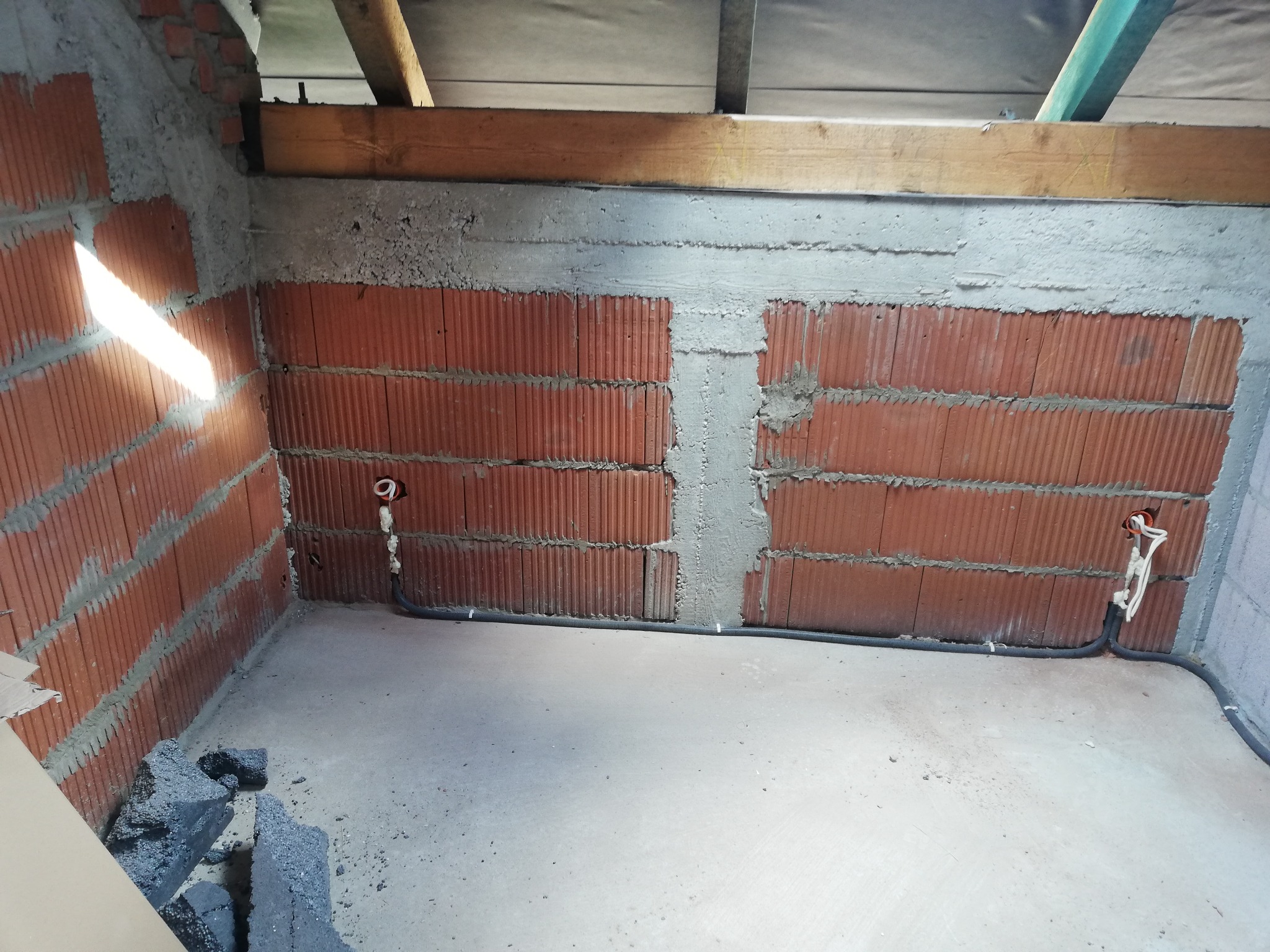 Surowy mur z cegły z widocznymi przewodami elektrycznymi w peszlu, przygotowany do tynkowania.