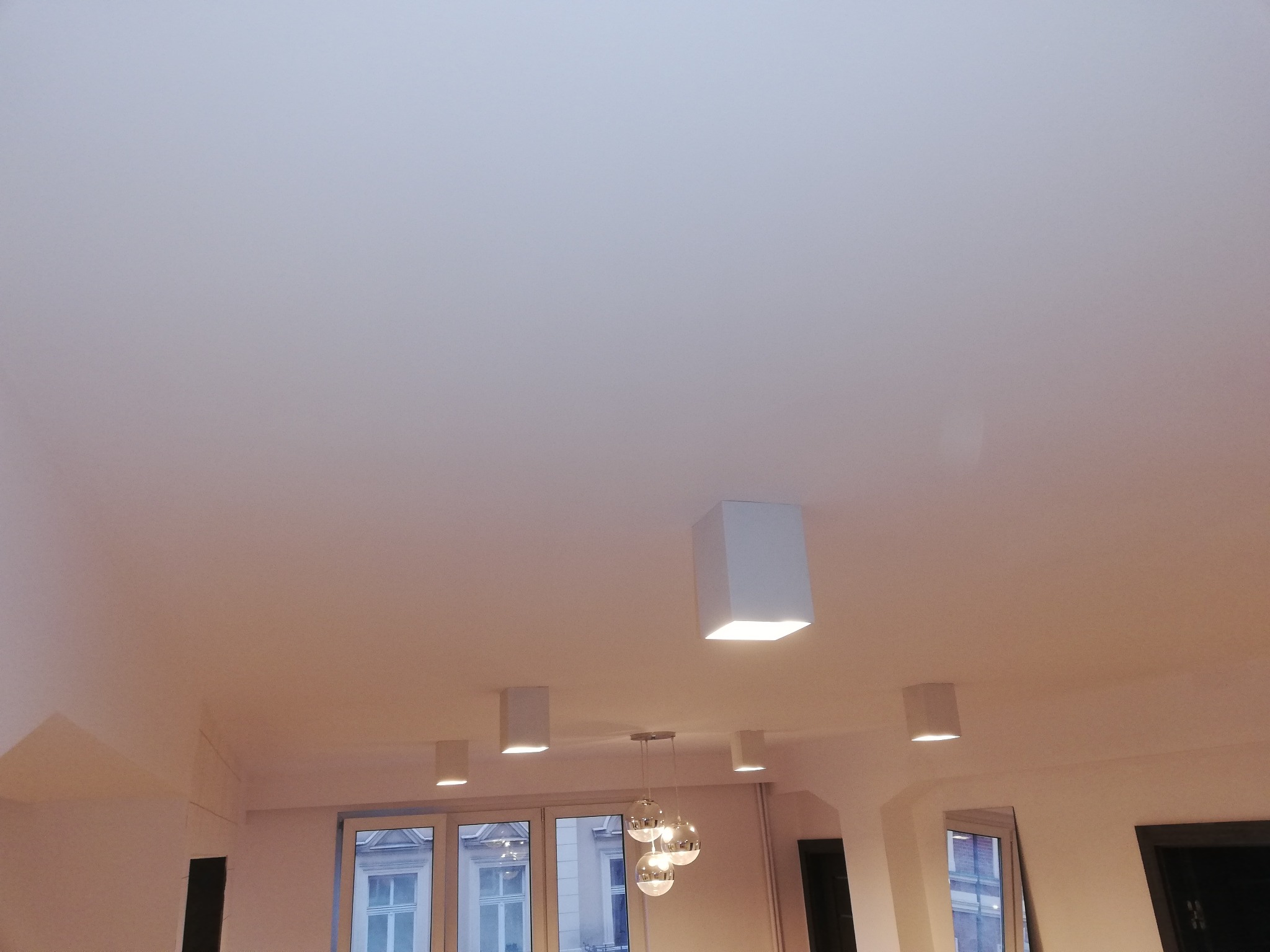 Biały sufit z zamontowanymi kwadratowymi lampami punktowymi LED i wiszącą lampą z kulistymi kloszami, widok z dołu.