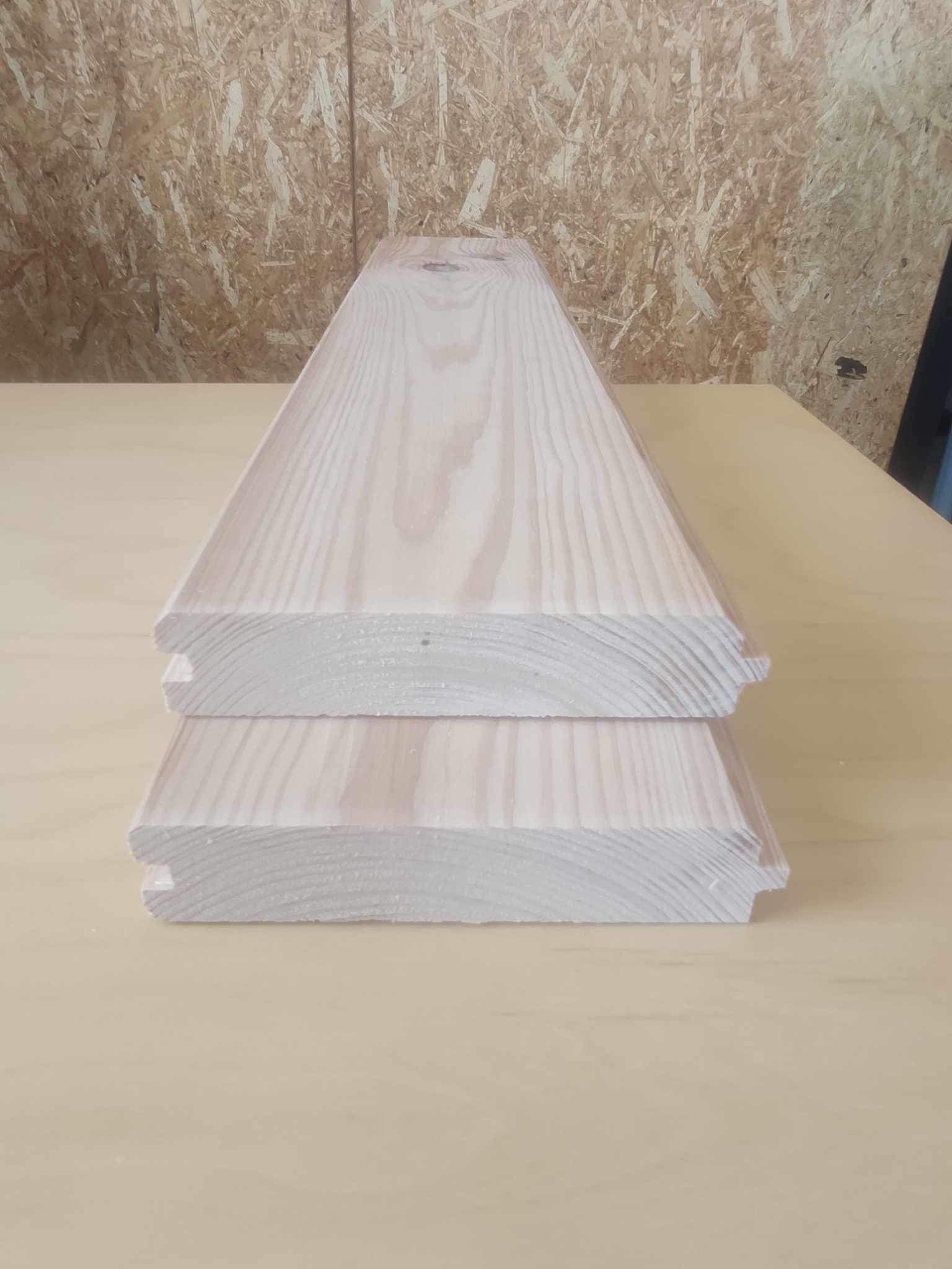 Dwie jasne deski podłogowe z wyprofilowanymi krawędziami, ułożone jedna na drugiej w Opalenicy, widoczne słoje drewna.