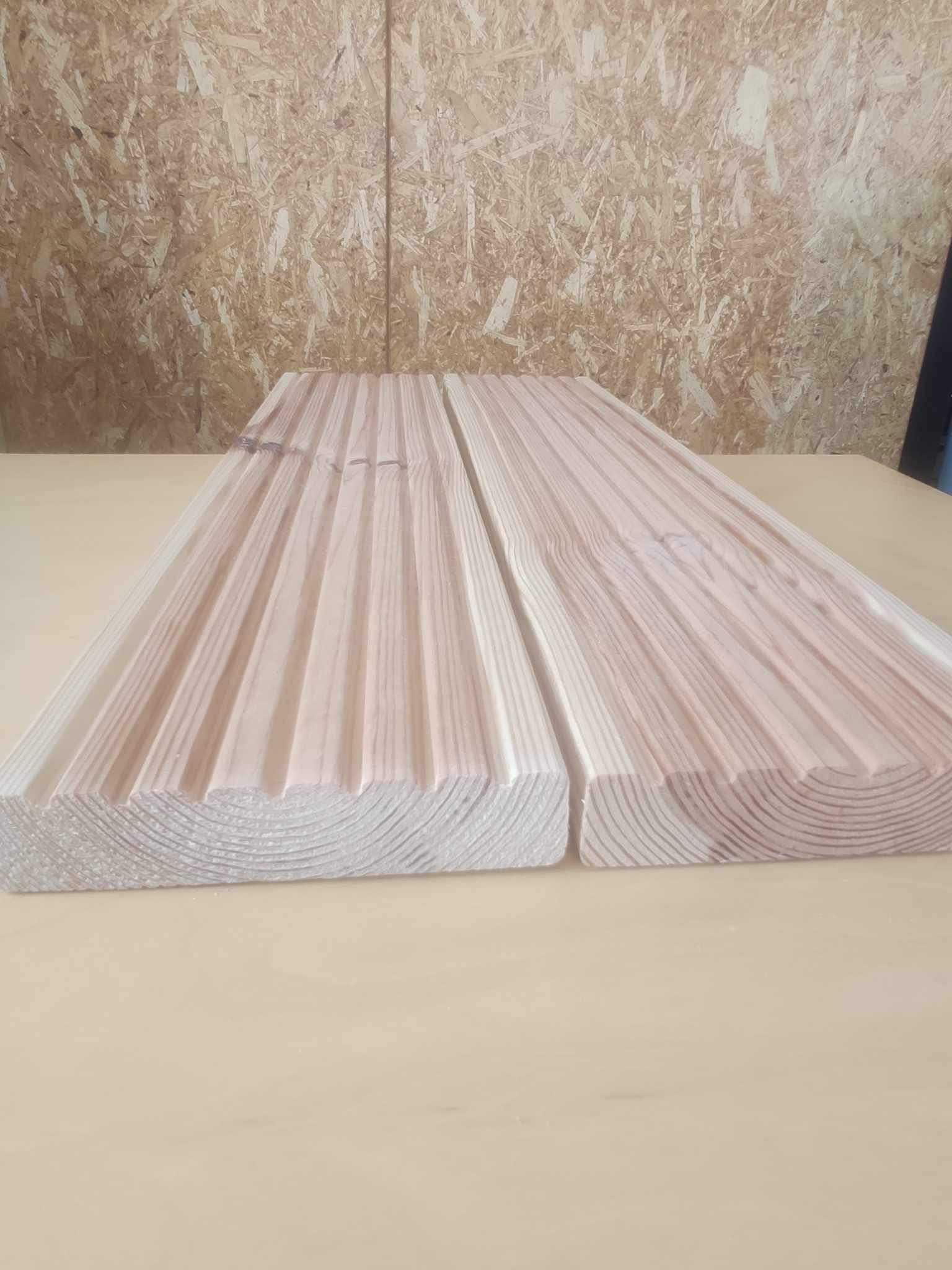 Dwie deski z frezowanymi rowkami, ułożone obok siebie na jasnym blacie, widoczny przekrój słojów drewna.