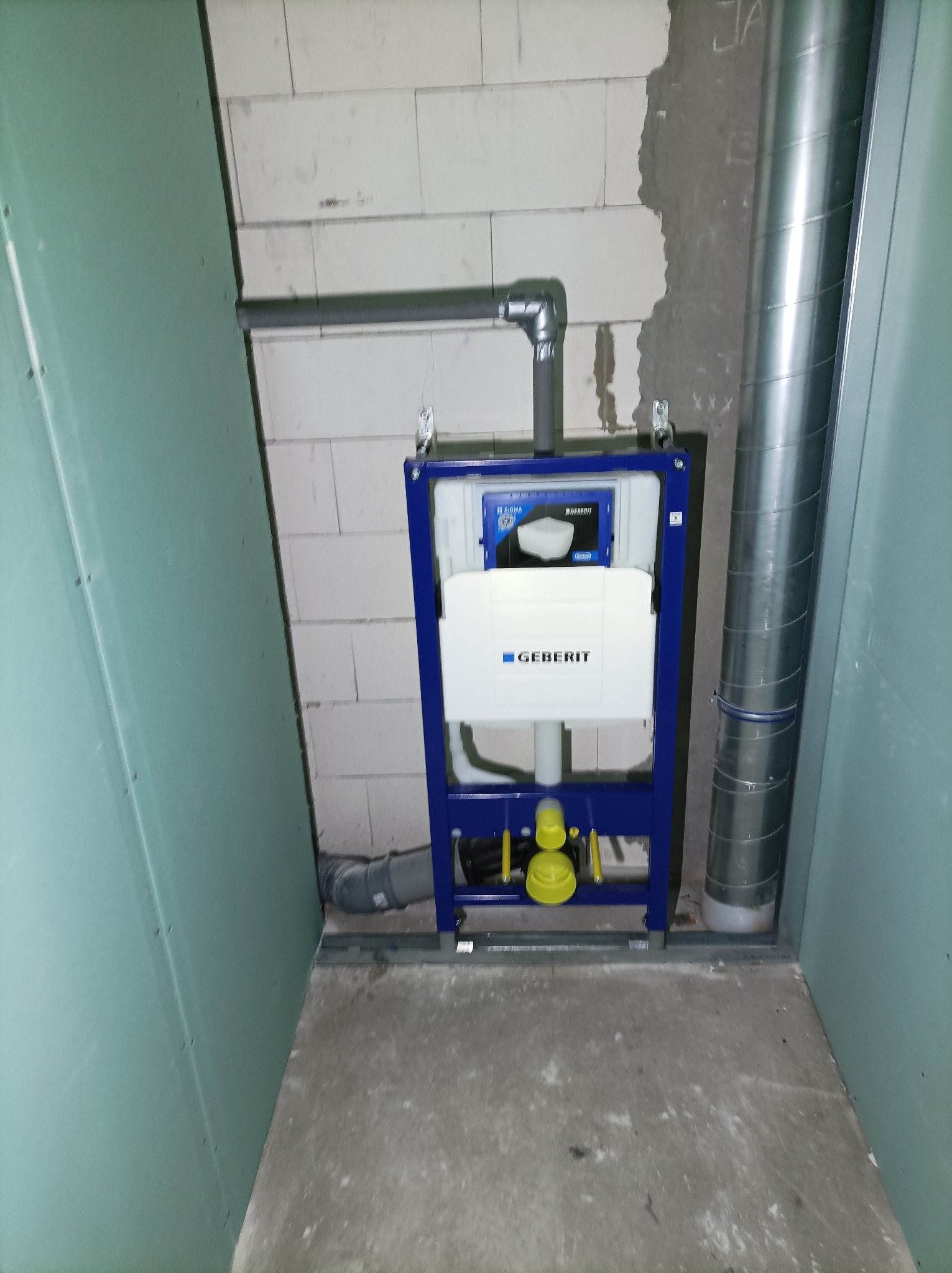 Stelaż podtynkowy Geberit zamontowany w surowej łazience, widoczne rury odpływowe i dopływowe, ściany w stanie deweloperskim: płyta gipsowo-kartonowa i bloczki betonowe.