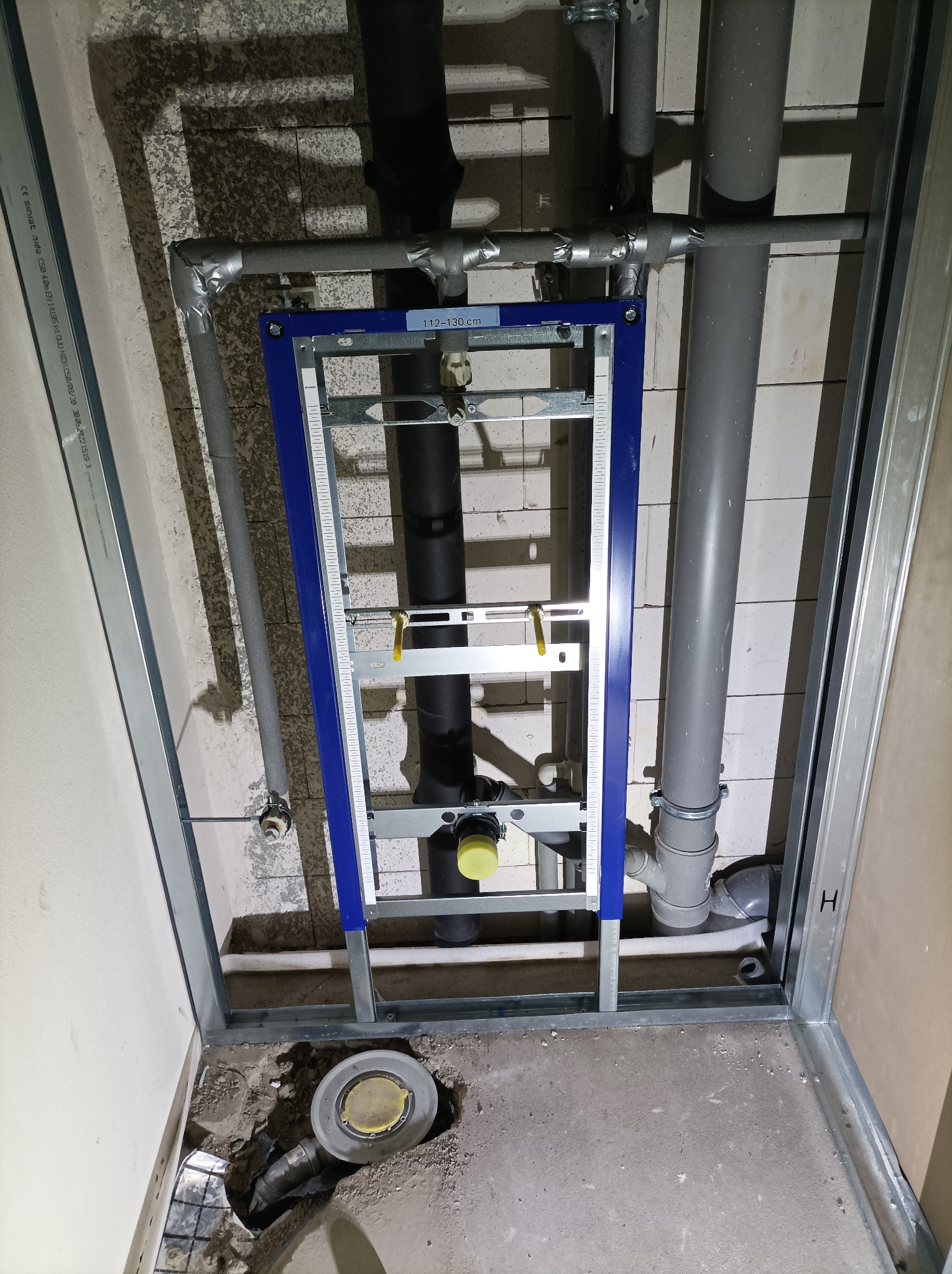 Stelaż podtynkowy WC zamontowany w łazience w trakcie remontu, widoczne rury kanalizacyjne i odpływ podłogowy, ściany w surowym stanie.