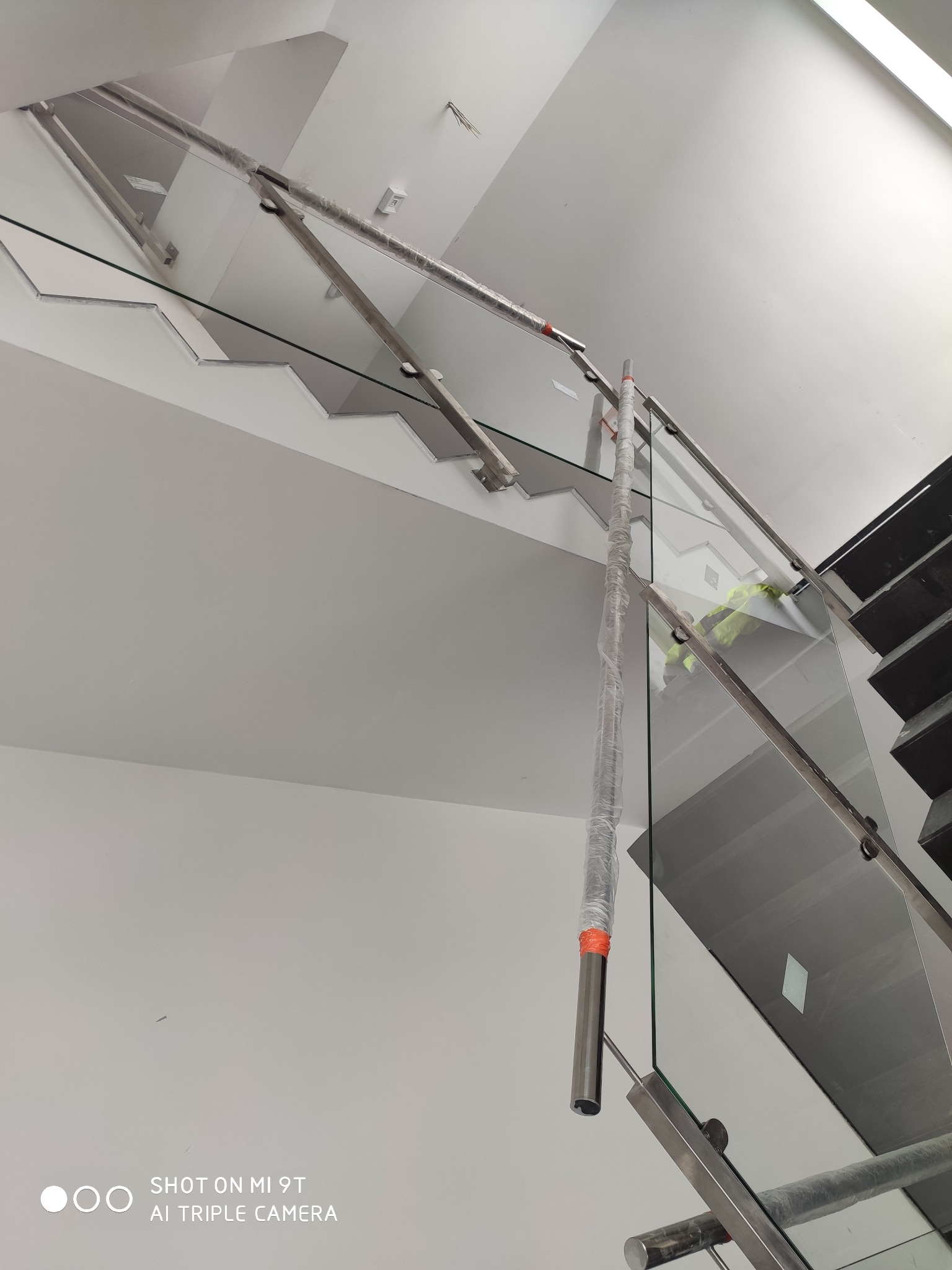 Szklana balustrada schodowa z elementami ze stali nierdzewnej, zabezpieczona folią ochronną podczas montażu, widok z dołu.