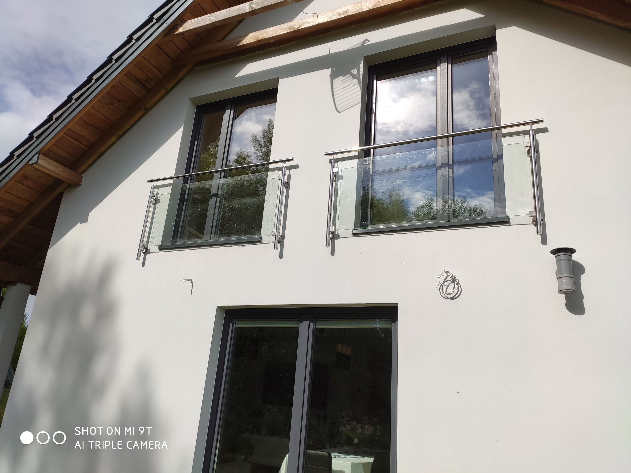 Nowoczesna fasada budynku z dwoma balkonami z szklanymi balustradami i nierdzewnymi poręczami, odbicie chmur w szybach.