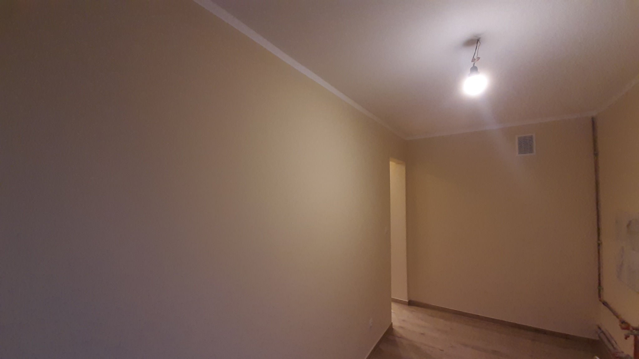 Jasne, świeżo pomalowane wnętrze z listwami przypodłogowymi i sufitowymi. Widoczna podłoga z paneli i proste oświetlenie sufitowe. Ściany w odcieniach beżu.