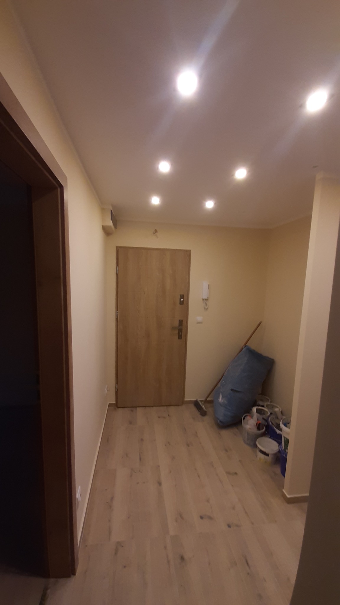 Jasne panele podłogowe w korytarzu po remoncie, widoczne puszki z farbą i narzędzia malarskie. Świeżo pomalowane ściany w odcieniach beżu.