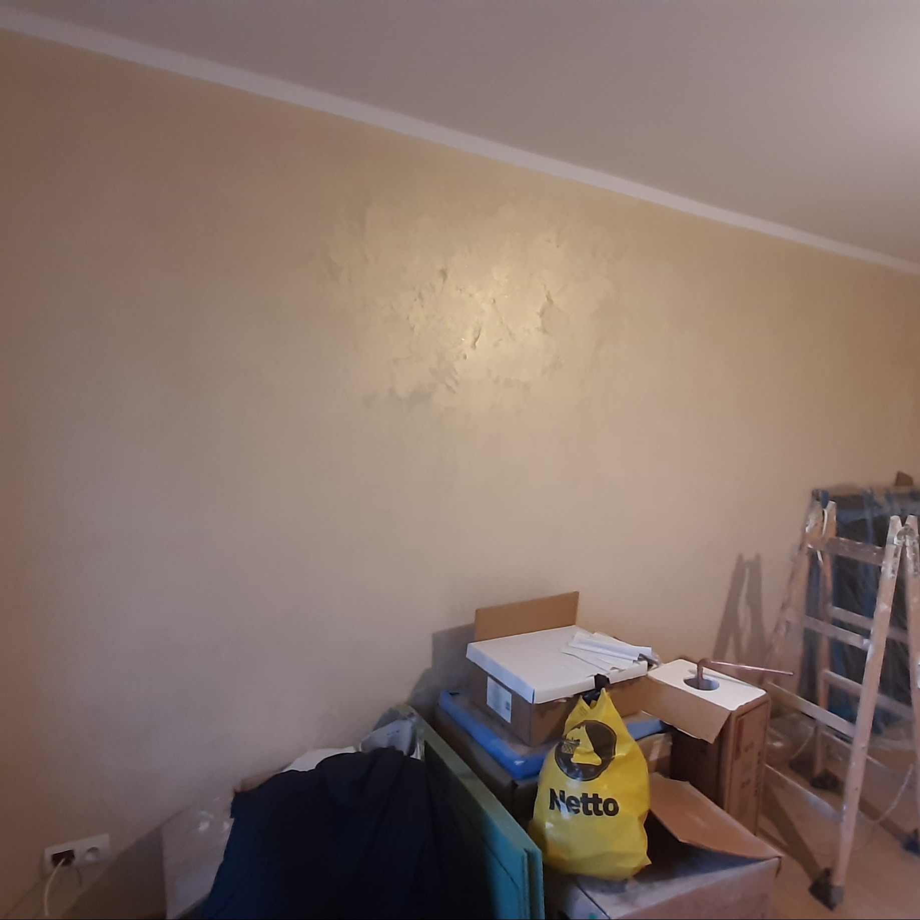 Beżowa ściana z dekoracyjną strukturą, widoczne narzędzia i drabina malarska. Wykończenie wnętrza z efektem 'chmurki'.