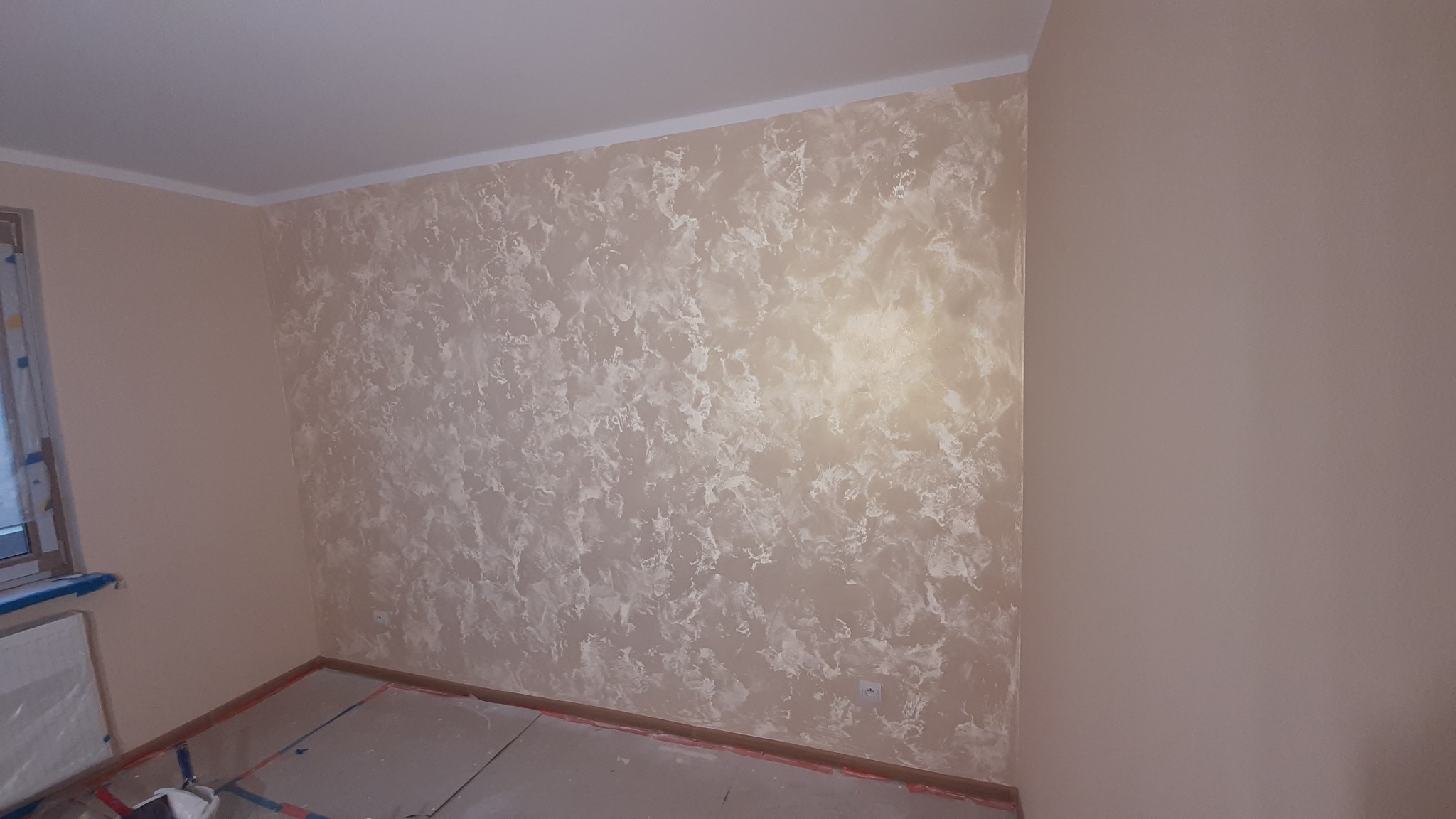 Pokój po malowaniu ścian z efektem dekoracyjnym. Widoczne gładkie ściany w odcieniach beżu i kremu, z unikalną teksturą przypominającą marmur. Podłoga zabezpieczona folią.