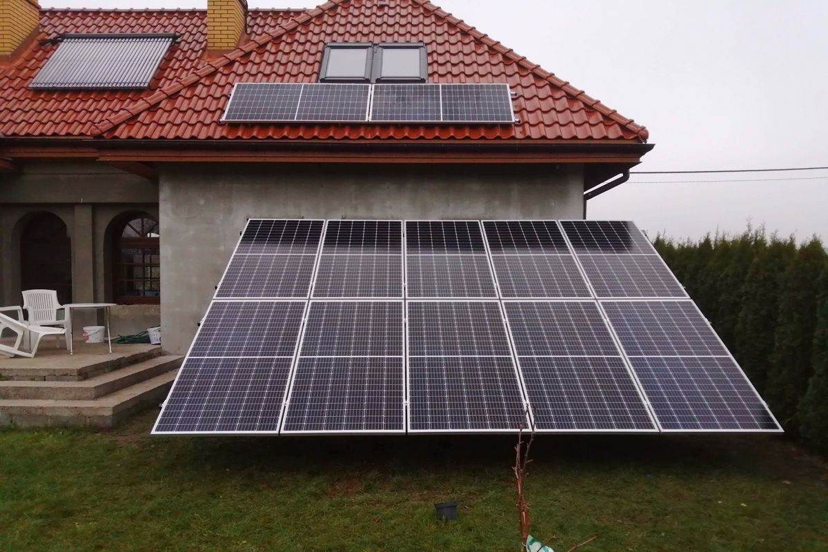 Instalacja paneli fotowoltaicznych na gruncie obok domu jednorodzinnego we Włocławku, widoczne również panele na dachu.