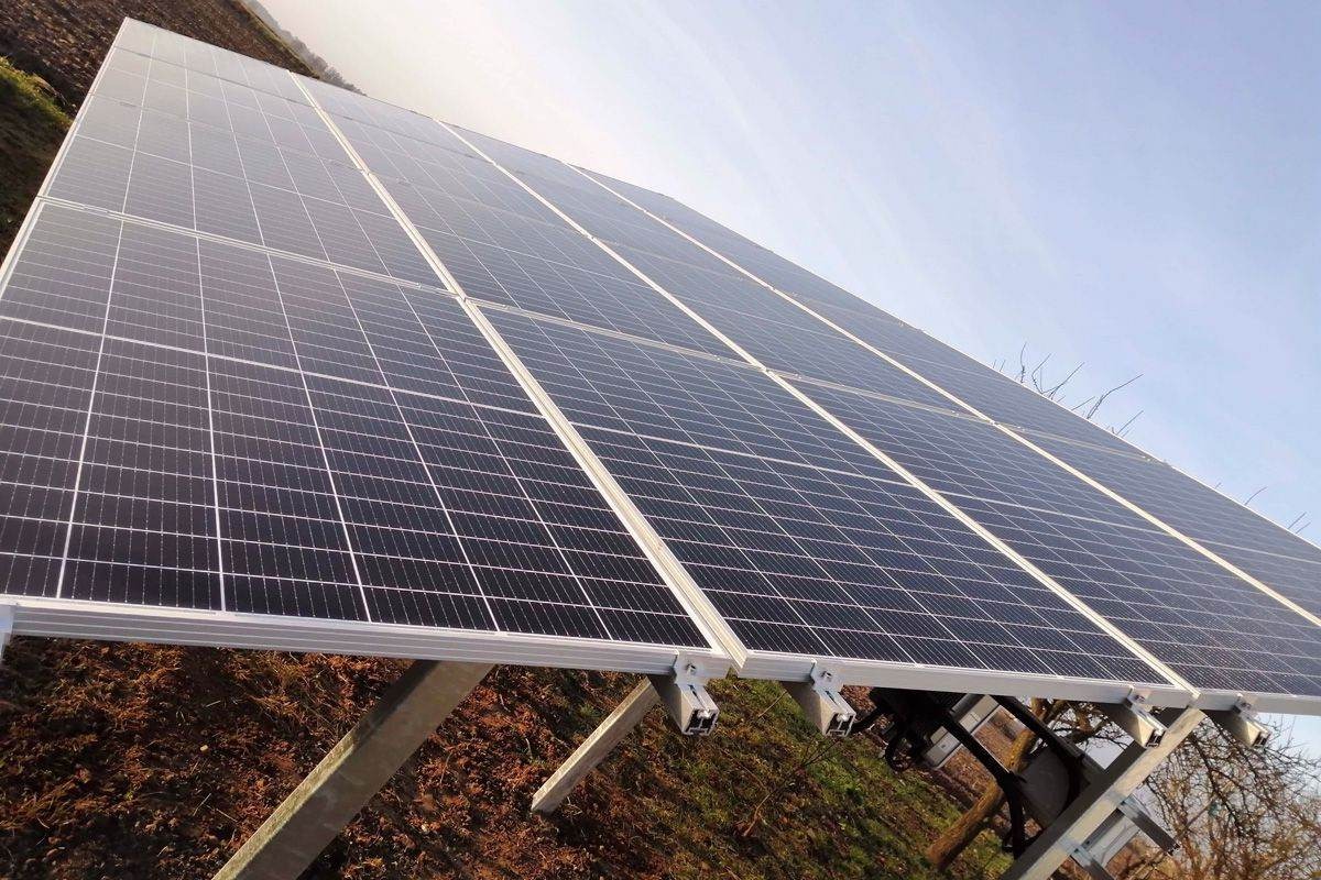 Panel słoneczny zamontowany na metalowej konstrukcji na tle pola i nieba, widok z dołu pod kątem.