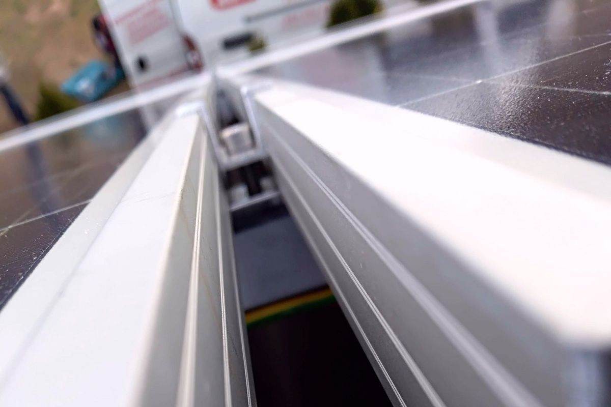 Szczegółowe ujęcie paneli fotowoltaicznych z widocznymi elementami montażowymi i fragmentem instalacji elektrycznej w tle, z perspektywy montażysty.