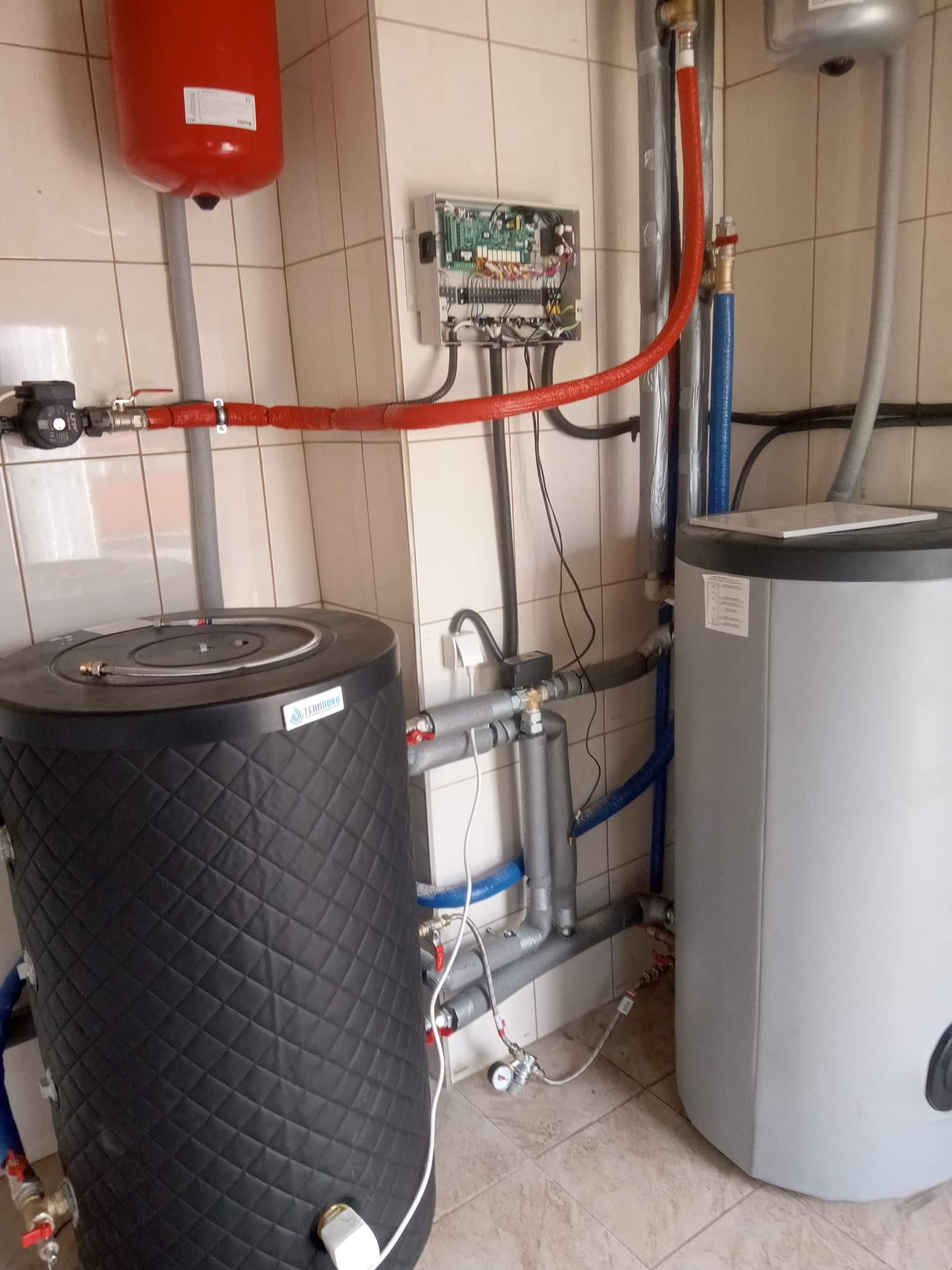 Instalacja z dwoma zbiornikami, czerwonym naczyniem wzbiorczym i panelem sterowania na tle beżowych płytek.