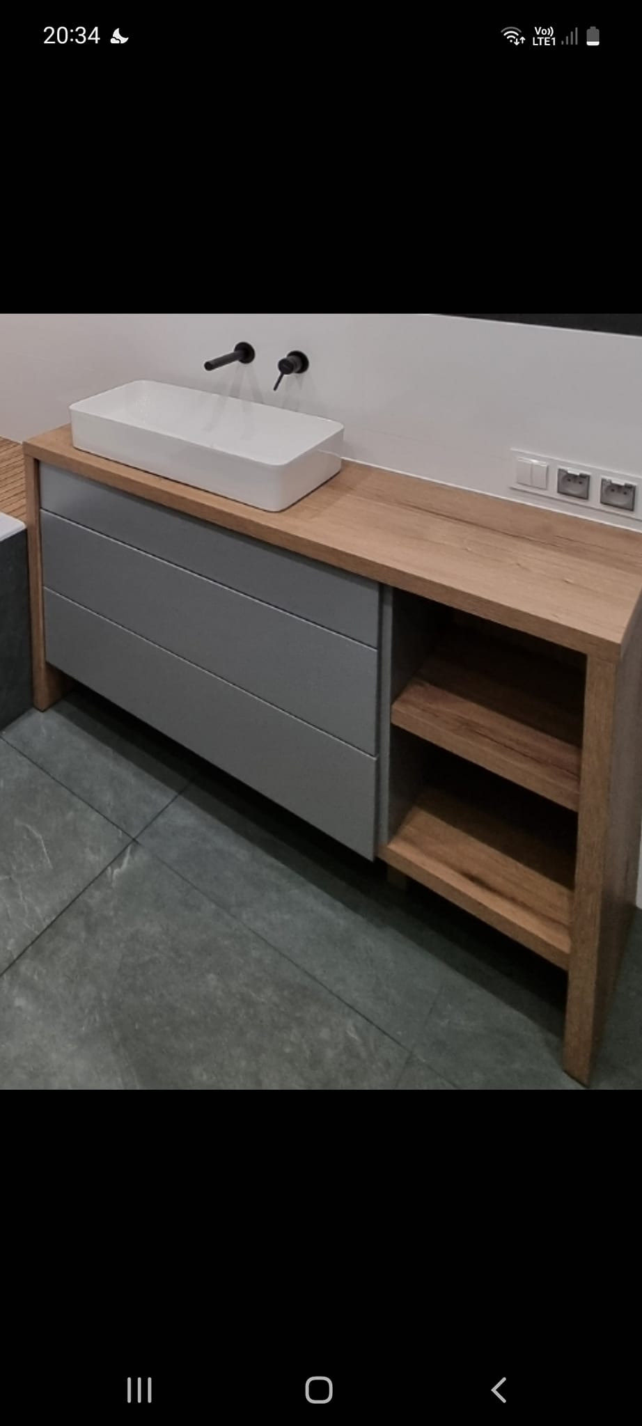 Nowoczesna łazienka z umywalką nablatową, szarą szafką z szufladami i drewnianym blatem z otwartymi półkami.