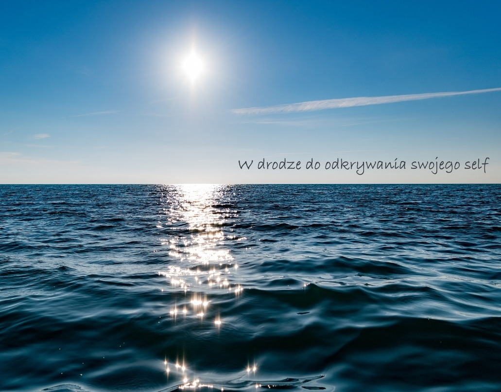 Spokojne, błękitne morze pod jasnym słońcem, z napisem 'W drodze do odkrywania swojego self' unoszącym się nad powierzchnią wody.