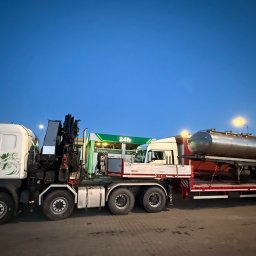 HDS Niepolomice - Ciężarówka z dźwigiem i cysterną na lawecie, zaparkowana przy stacji benzynowej o zmierzchu. Widoczny biały ciągnik siodłowy z zielonymi detalami i czarny dźwig.