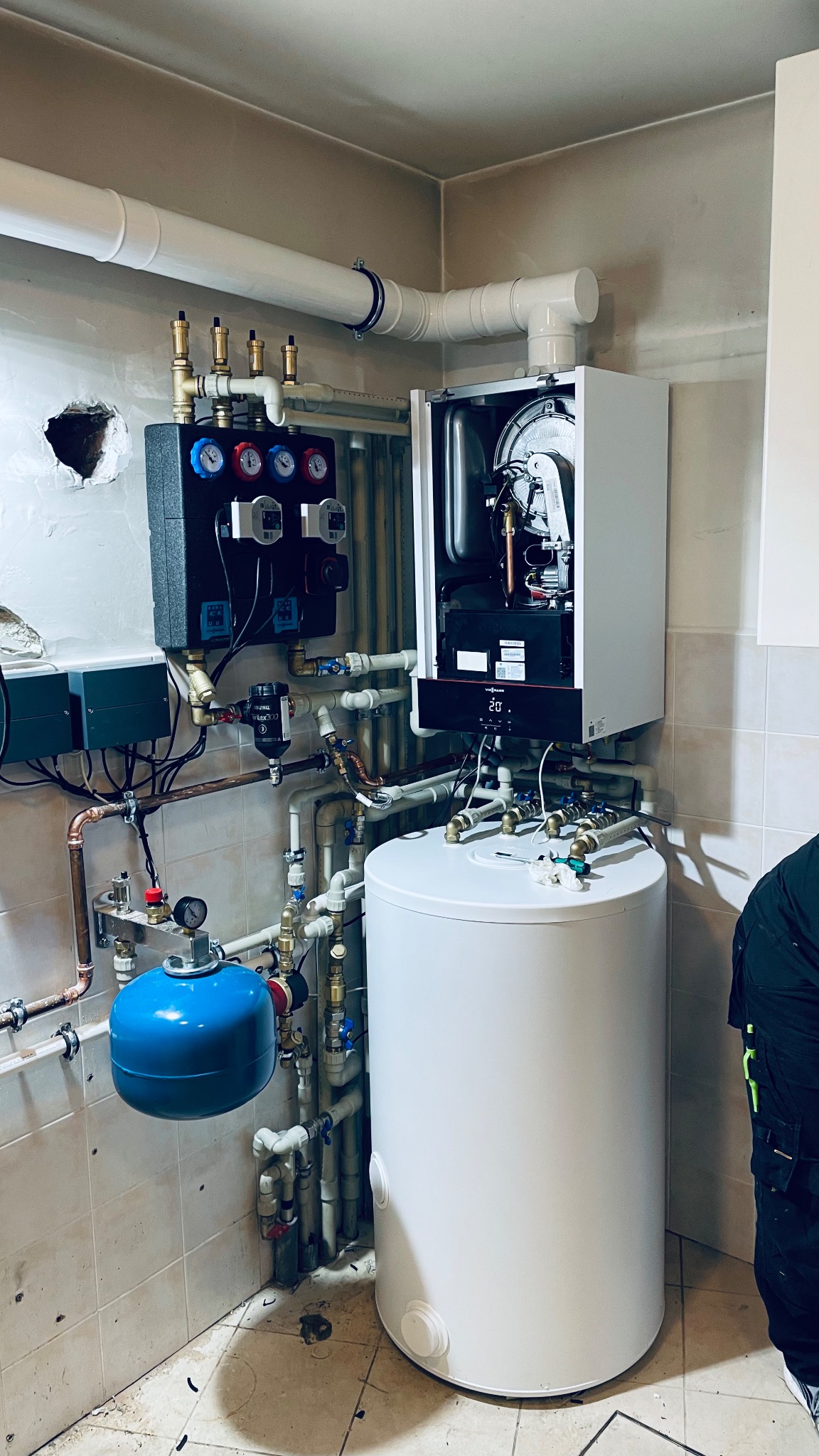 Kotłownia z zamontowanym piecem gazowym Viessmann, zbiornikiem na wodę i rozbudowaną instalacją hydrauliczną. Widoczne liczne rury miedziane i plastikowe, manometry oraz niebieskie naczynie...